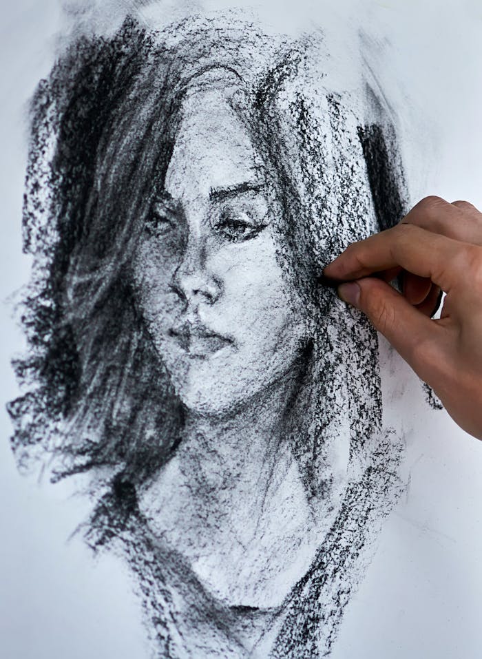 headline An artist's hand sketching a charcoal portrait of a woman on paper.